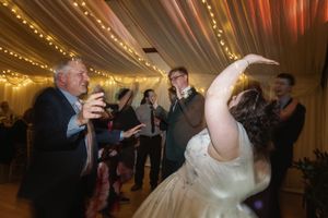 Wedding reception guests dance and celebrate under twinkling string lights in a decorated venue.