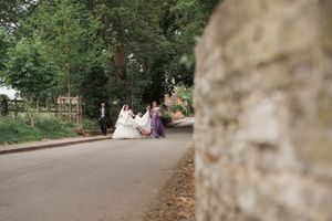 Wedding party walking down a tree-lined path in an outdoor garden setting.
