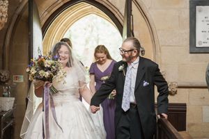 Wedding party exits through stone church archway with celebratory expressions.
