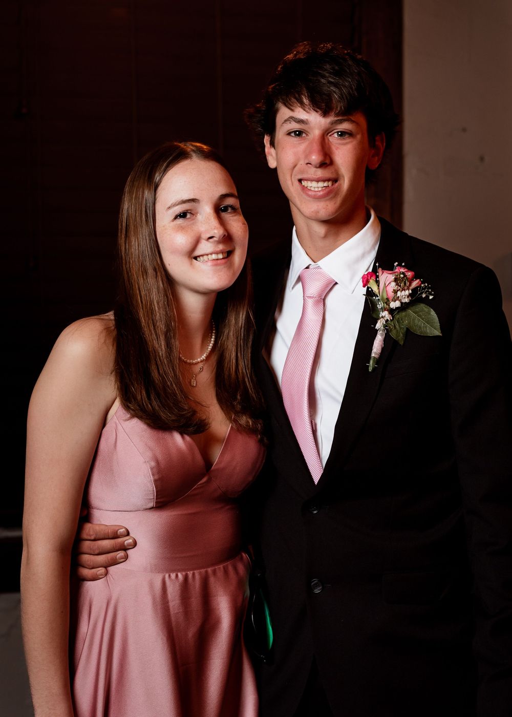 A couple dressed for a formal event with one person in a black suit and pink tie and the other in a pink dress.