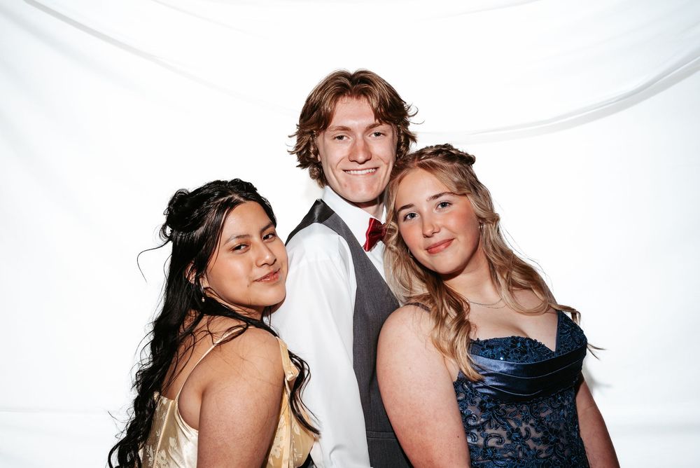 Three people in formal attire smile and pose together against a white backdrop at a special event.