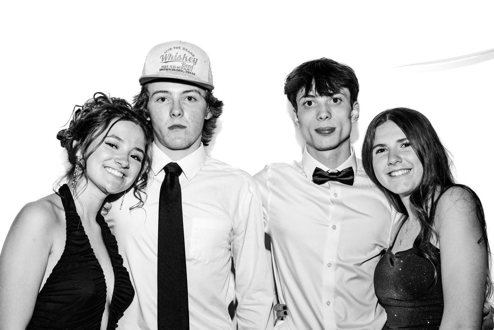 Black and white photo of four people posing together at a party in fun formal attire.