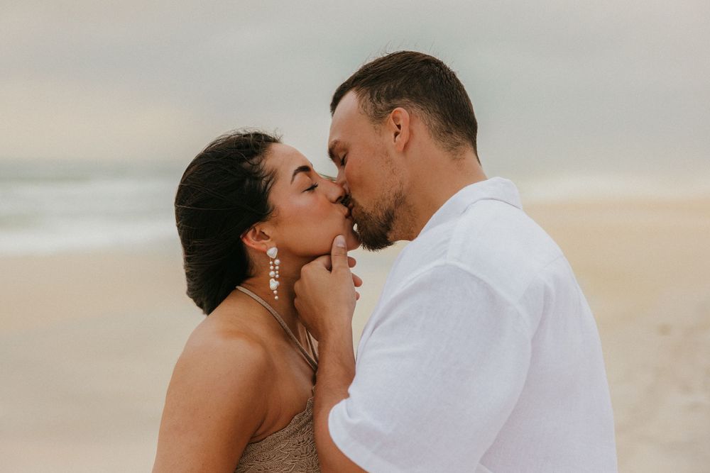 Romantic couple sharing an intimate kiss on a sandy beach during sunset.