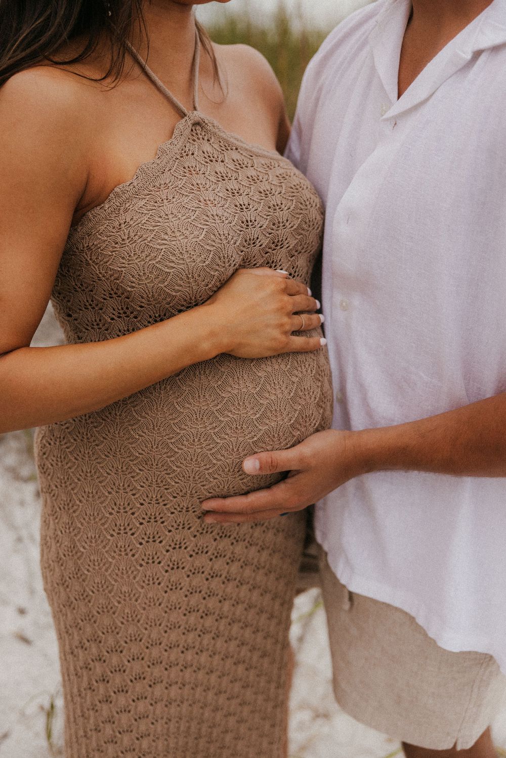 Close up of a maternity photo showing a couple embracing with hands on a textured tan dress.