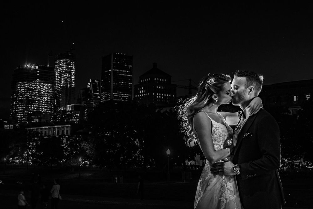 A couple shares an intimate moment at night with a city skyline of illuminated buildings providing a romantic backdrop.