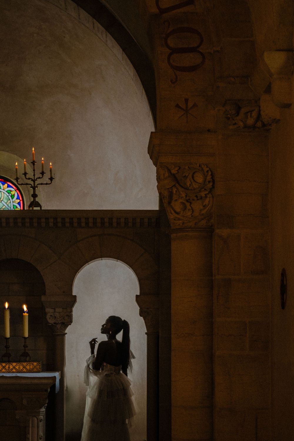 Silhouette in a dramatic archway of a historic church interior with stained glass and candlelight casting warm shadows.