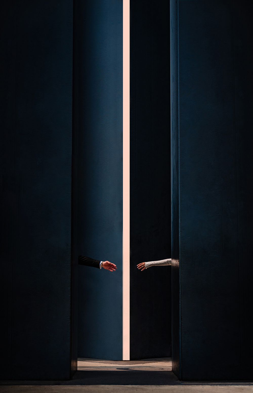 A dark surreal scene showing hands reaching through a vertical crack illuminated by a bright light line.