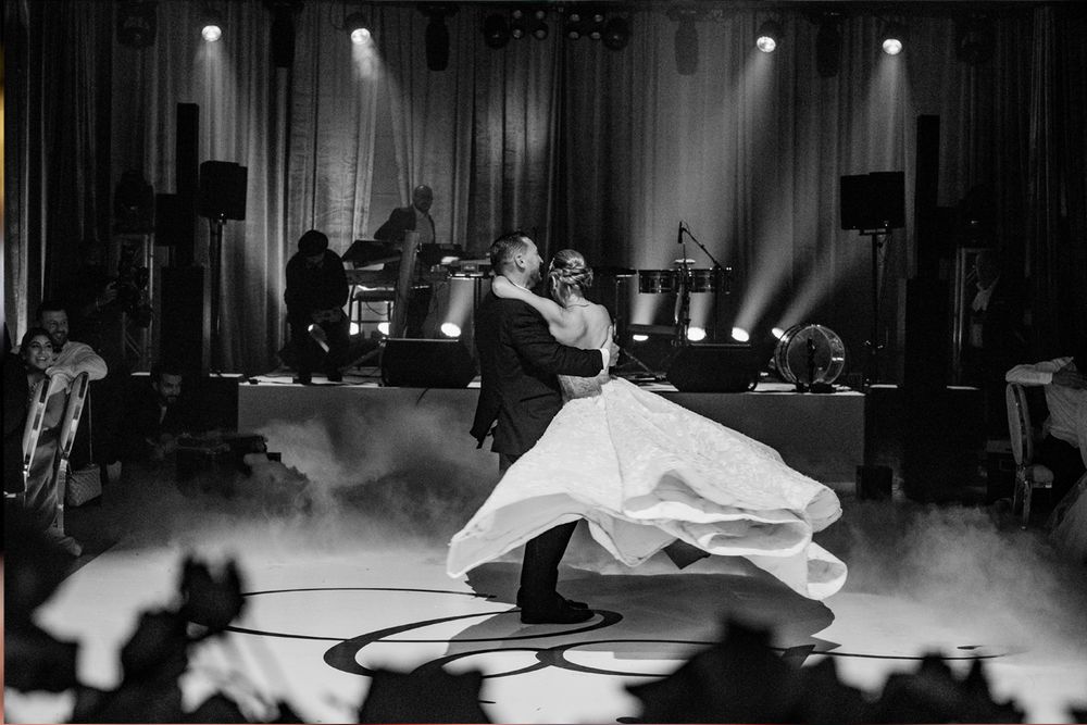 A couple performs an elegant dance move on a misty stage during what appears to be their first wedding dance.