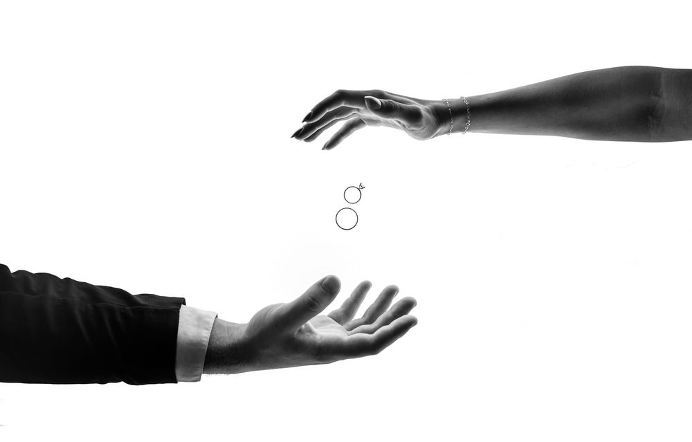 Black and white image of two hands reaching towards each other with wedding rings between them.