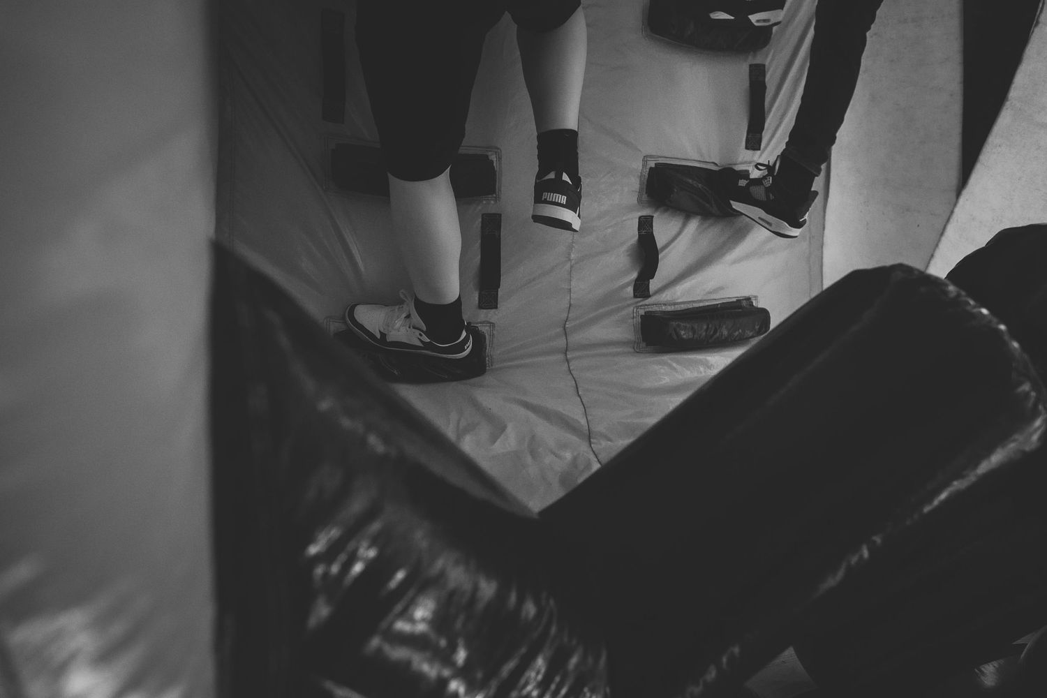 Black and white view of legs wearing casual shoes climbing in a bouncy obstacle course.