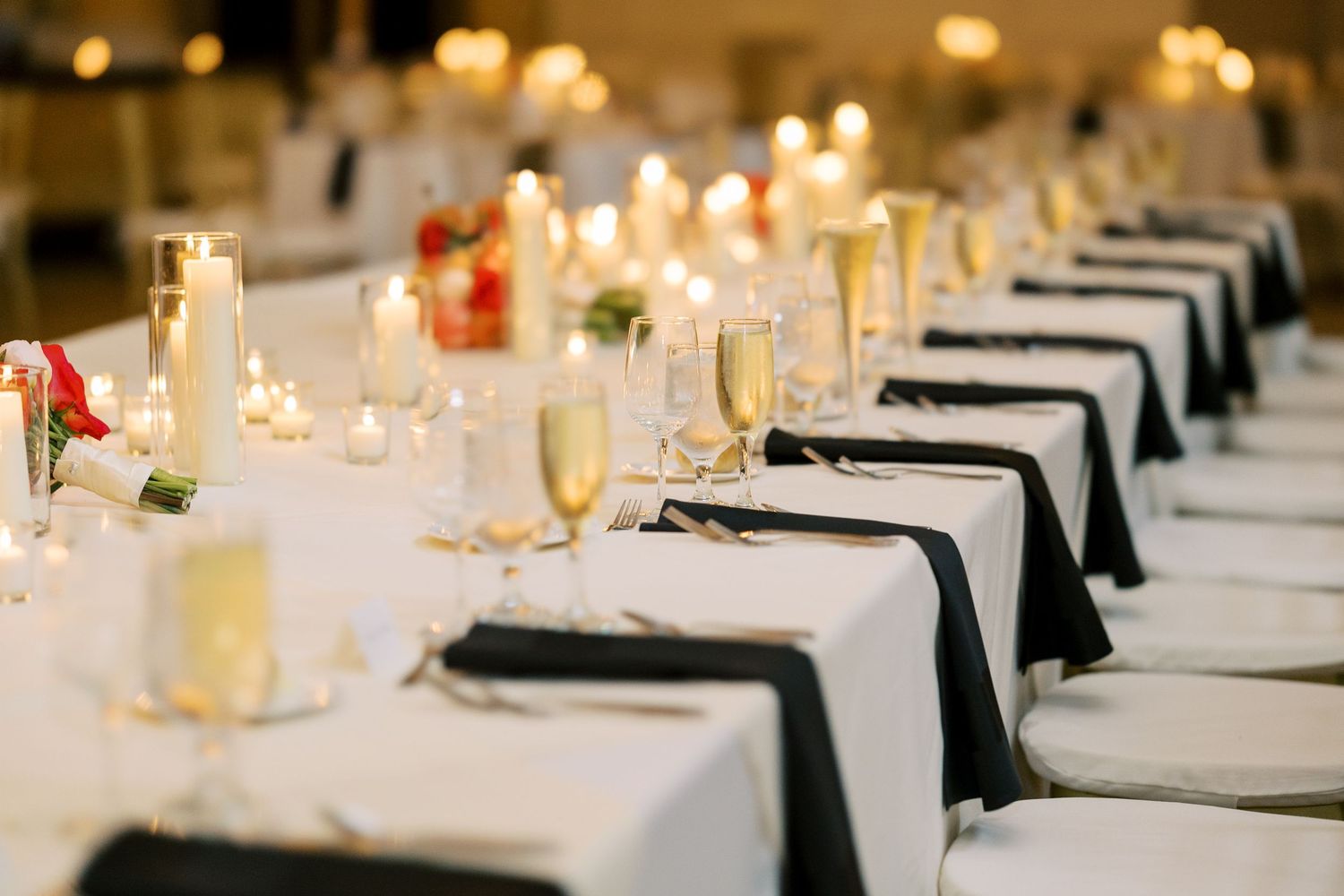 Long dining table set with white linens, black napkins, lit candles, and glassware for an elegant formal event at Hall of Springs.