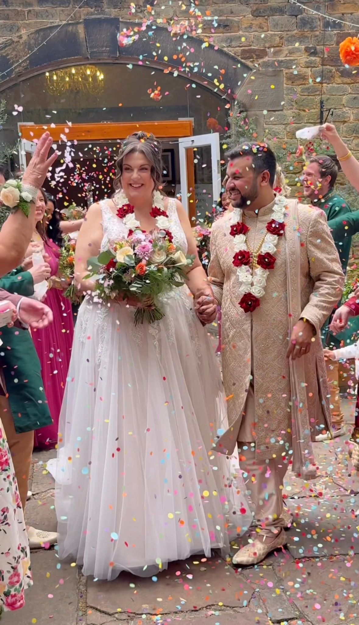 Bride and groom walking through their bright coloured confetti tunnel with big smiles on their faces.
