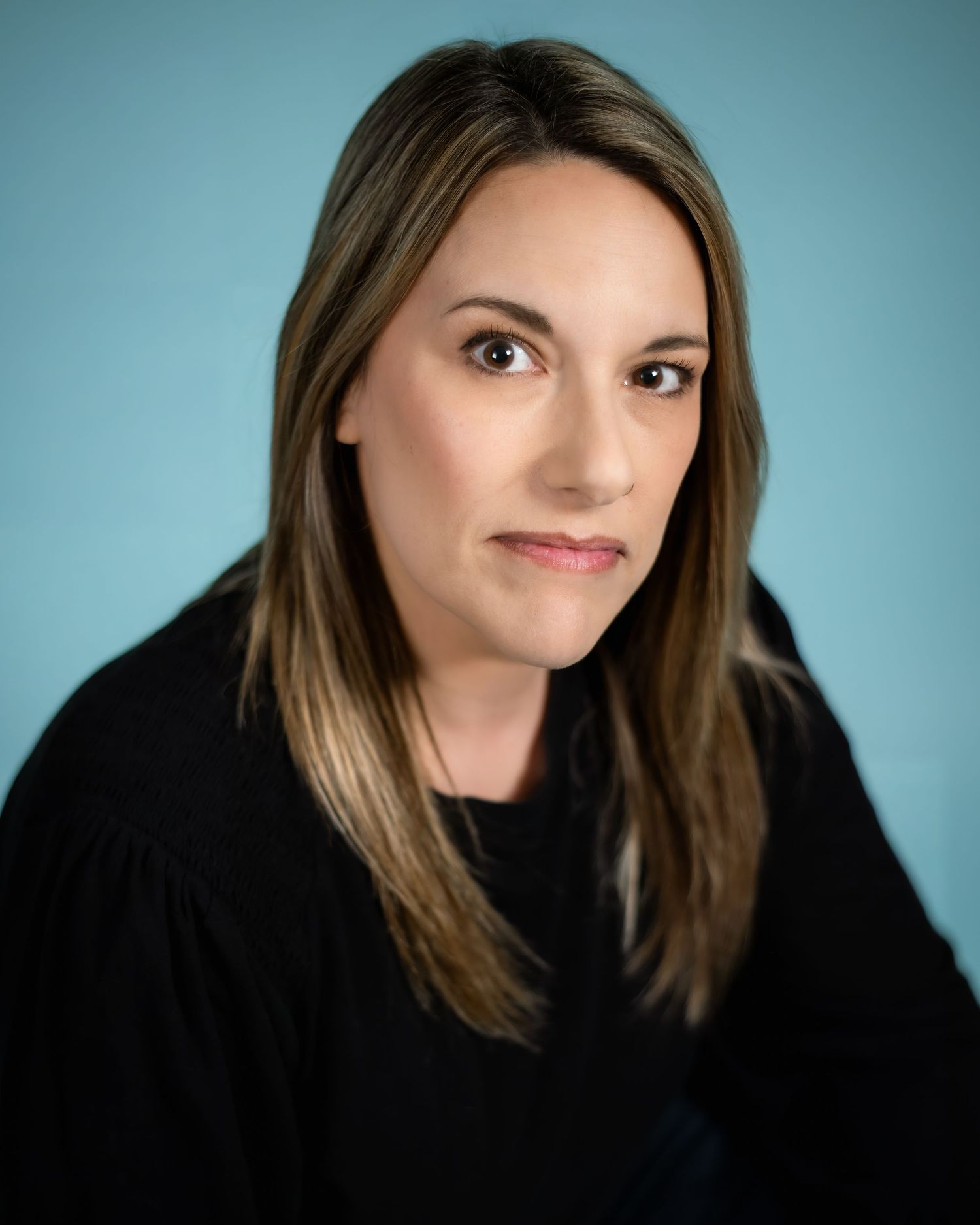 Professional studio portrait of someone in a black sweater against a teal background with soft lighting.
