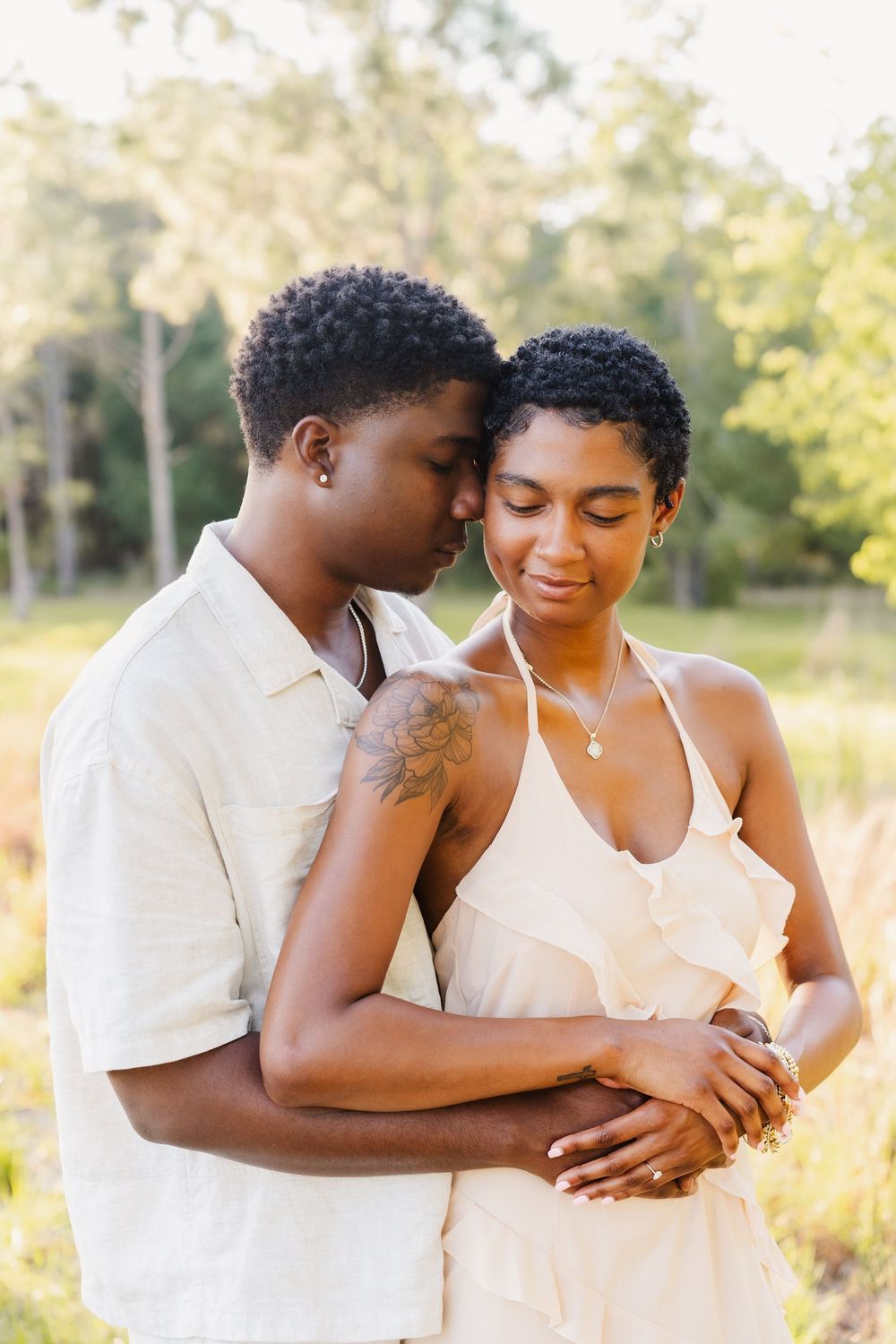A romantic couple in white outfits embrace tenderly in a sunlit meadow during golden hour.