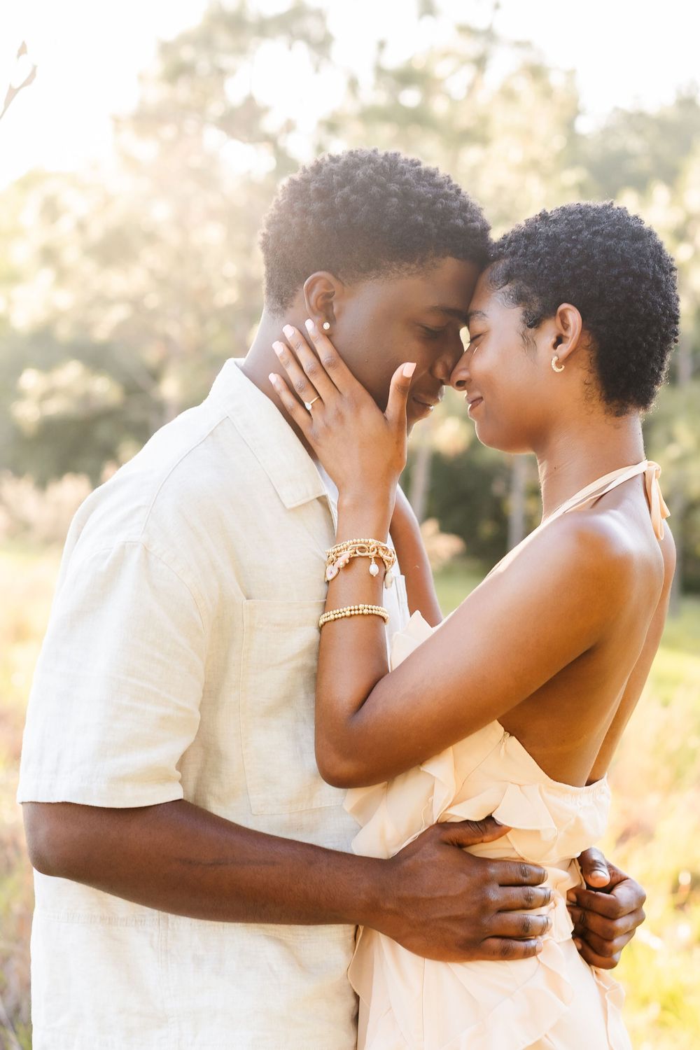 Intimate couple sharing tender moment outdoors in warm sunlight wearing light summer attire.