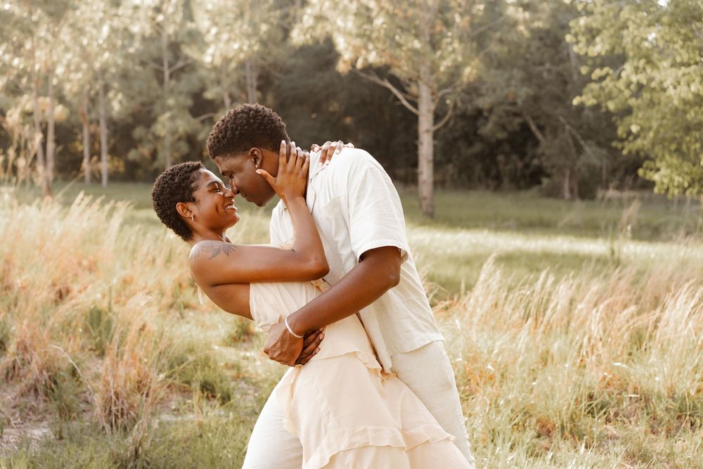 A couple shares an intimate moment in a sun-drenched field of tall grass during golden hour.