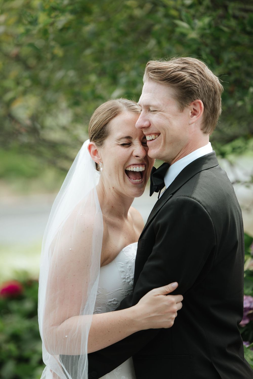 A happy couple shares joyful laughter and tender moments during their outdoor wedding photoshoot in a garden setting.
