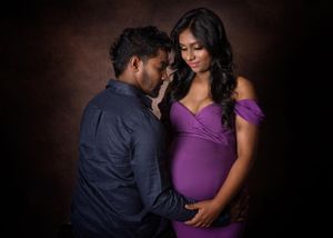 Maternity portrait of a couple, pregnant woman in a purple dress.