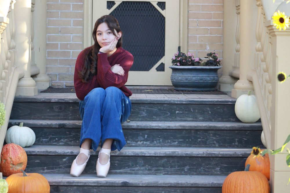 Autumn scene with person sitting on porch steps decorated with pumpkins and fall decor.