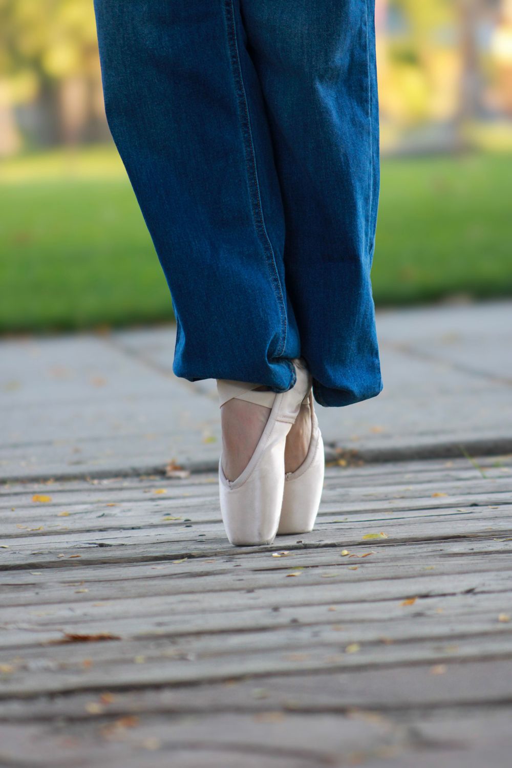 Close-up of ballet pointe shoes and blue jeans on wooden deck.