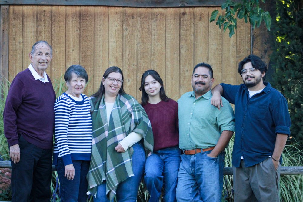 Family of six poses together outdoors wearing coordinated casual clothing against wooden wall.
