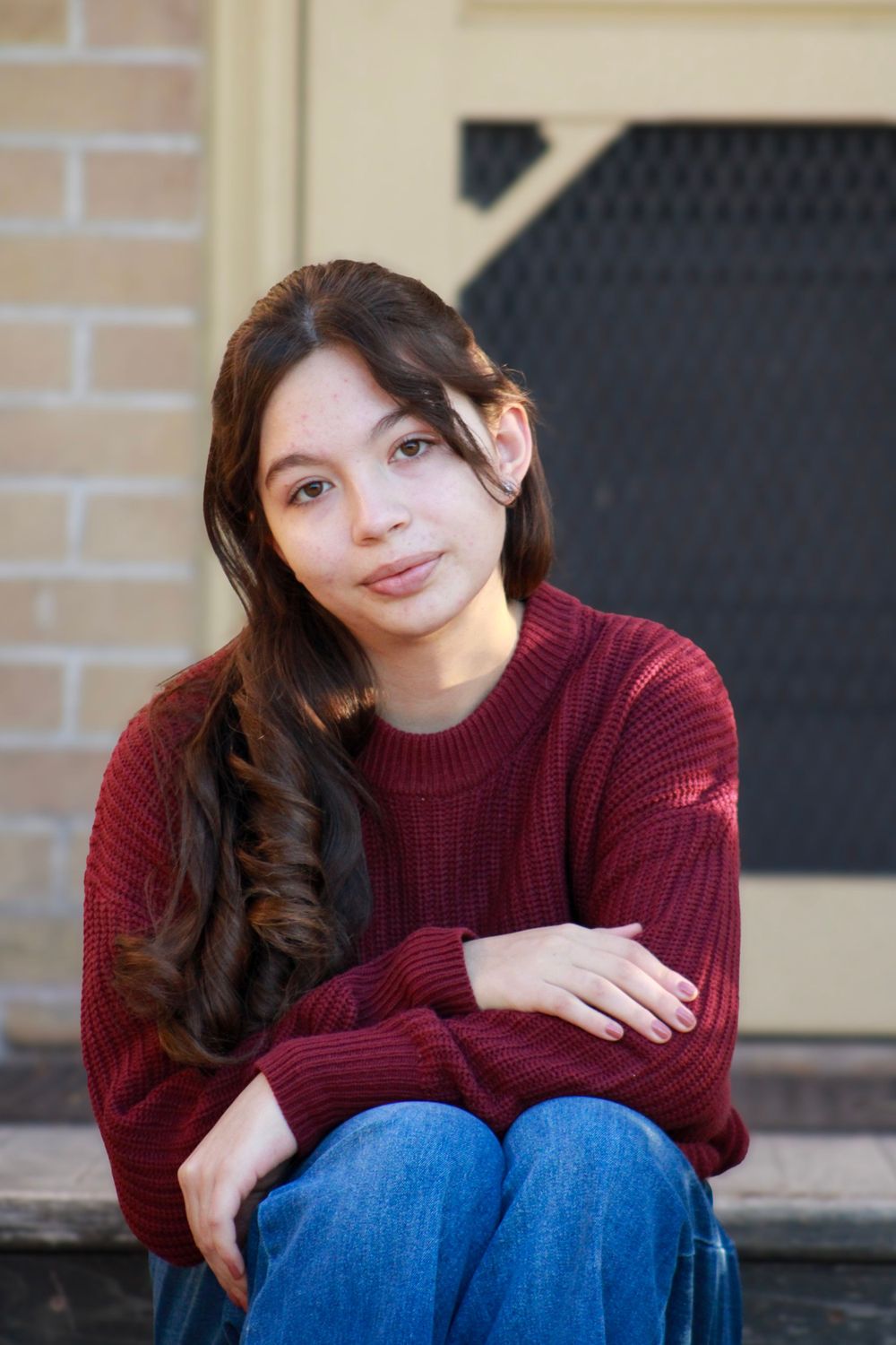 Portrait of person in burgundy sweater sitting relaxed on outdoor steps.