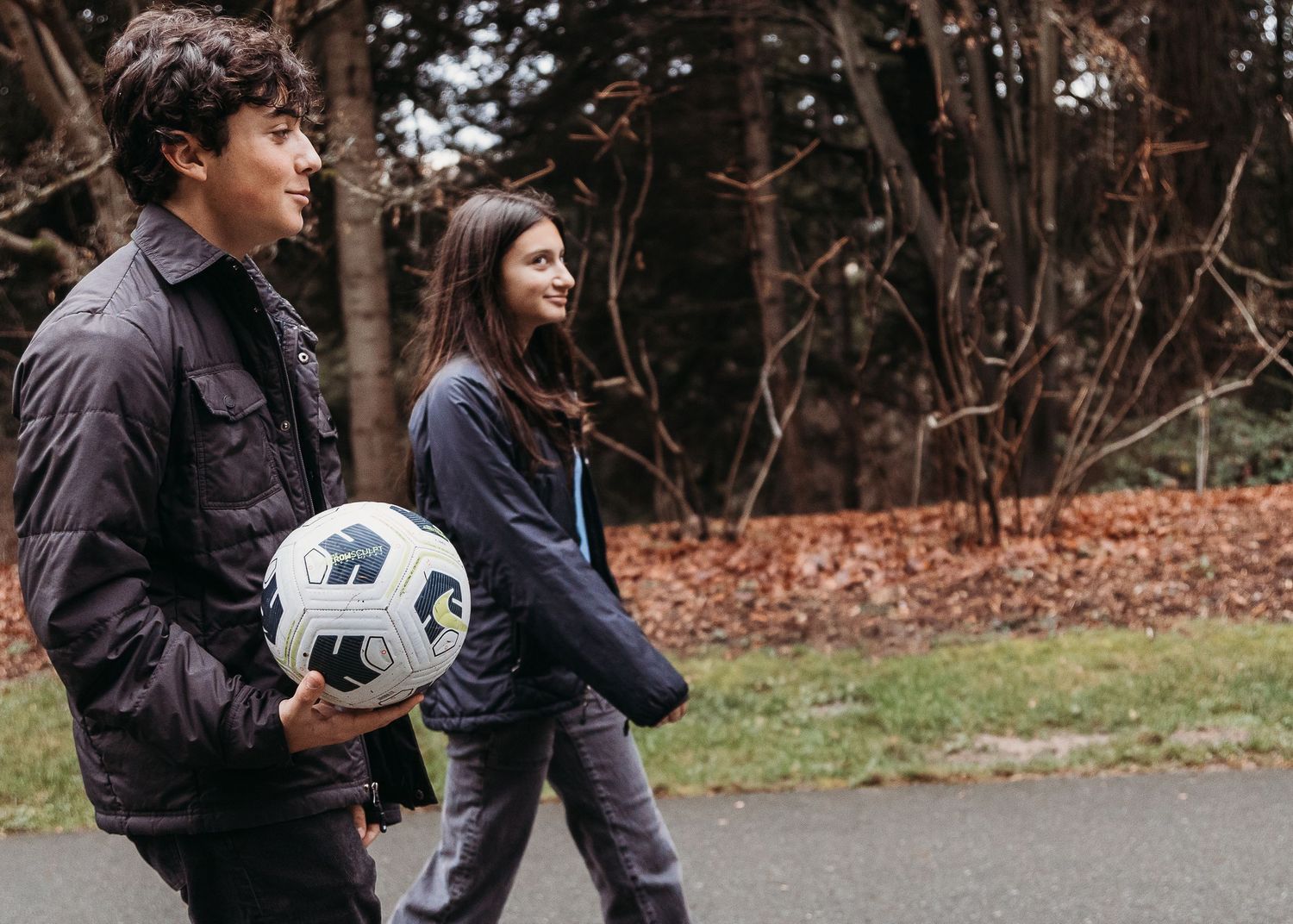 Couple walking outdoors in casual clothes with soccer ball in autumn setting.