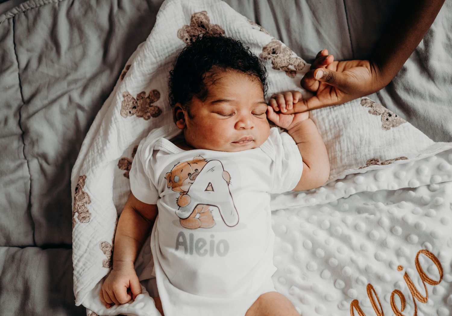 A sleeping baby wearing a letter A shirt rests on patterned bedding.