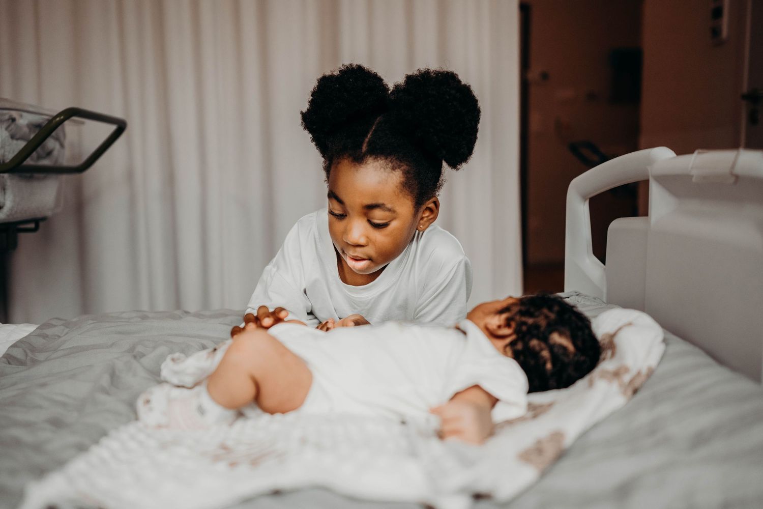 A tender moment showing a caregiver playing with a baby on a bed with white linens.