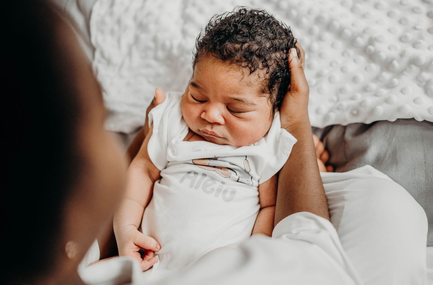 A sleeping baby in white clothing rests peacefully while being gently cradled.