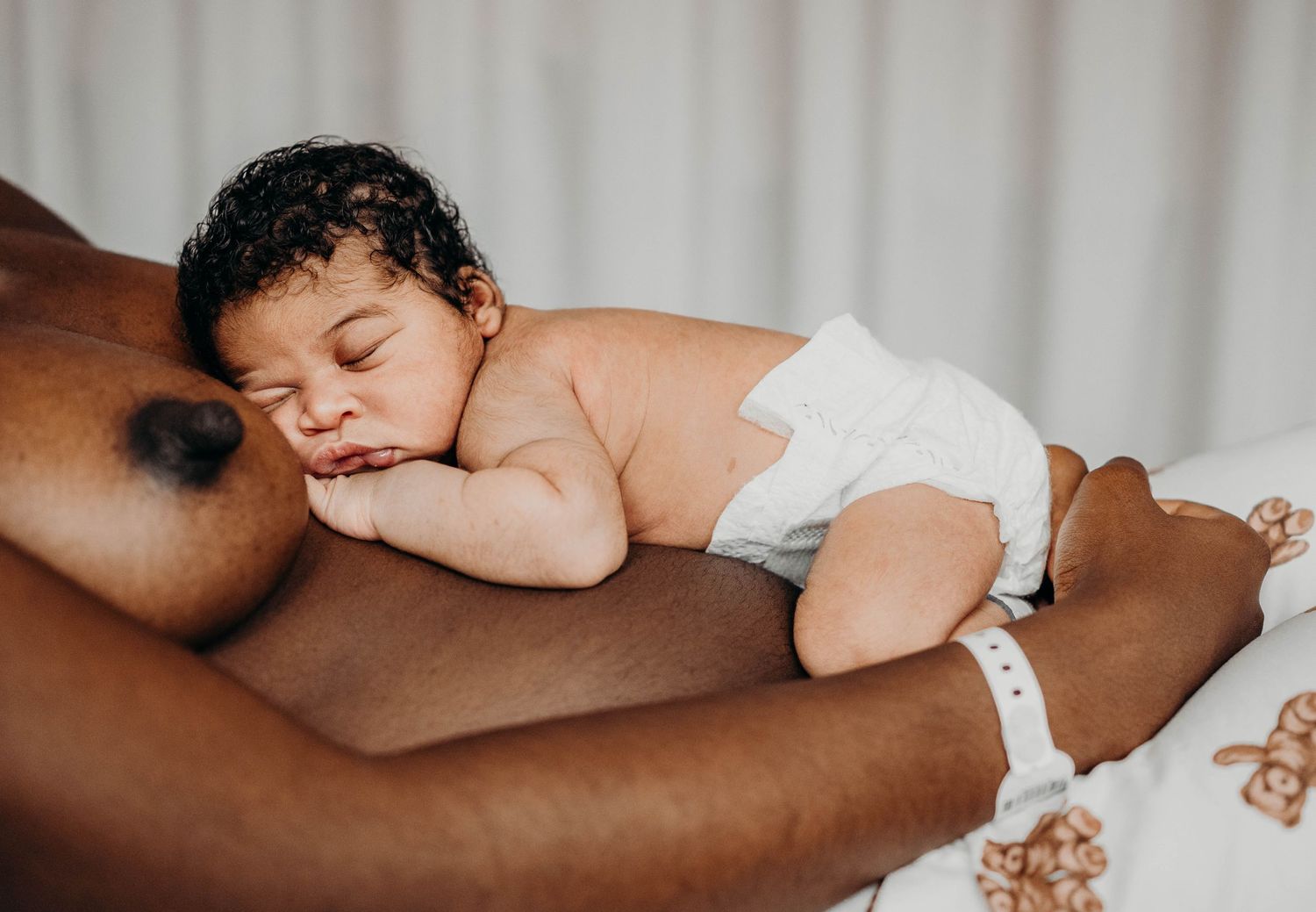 A sleeping infant in a white diaper rests peacefully on someone's lap.