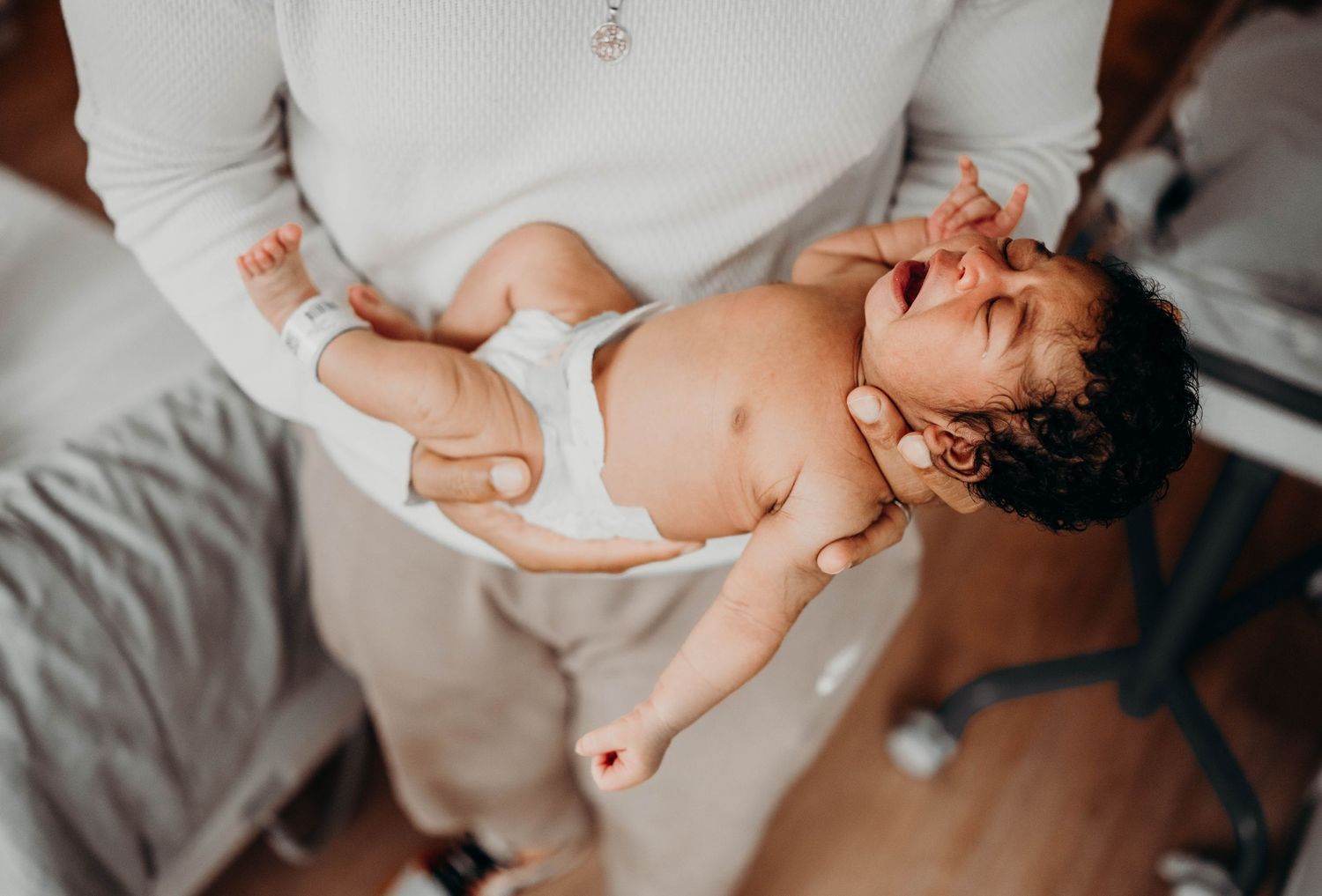 A small infant being held and cradled while wearing a white diaper.