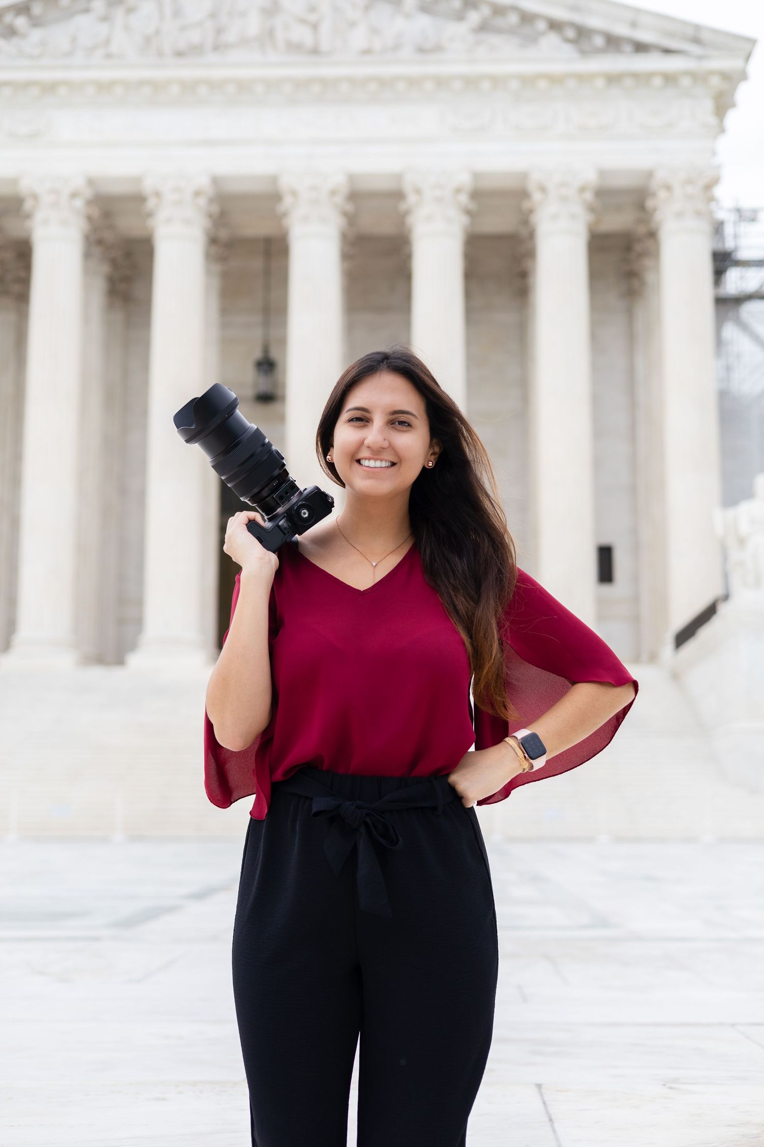 Professional photographer in burgundy top poses with camera at Supreme Court building.