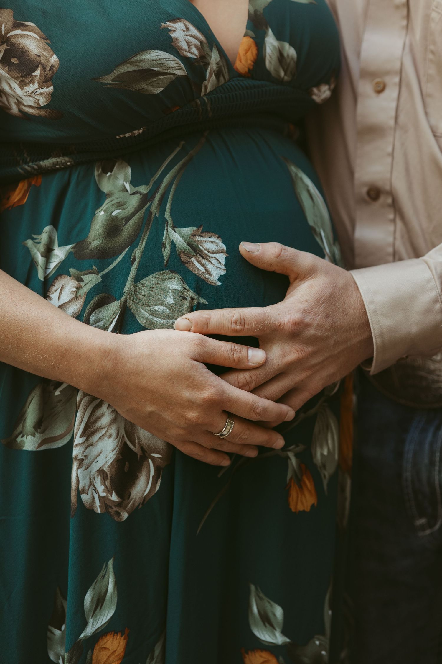 Close up of hands cradling pregnant belly in floral print dress.