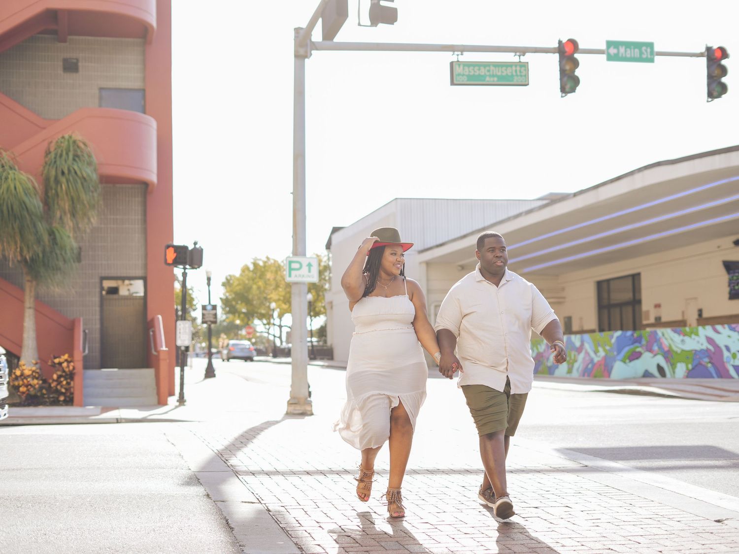 A couple in white outfits walking hand in hand on a sunny urban street.