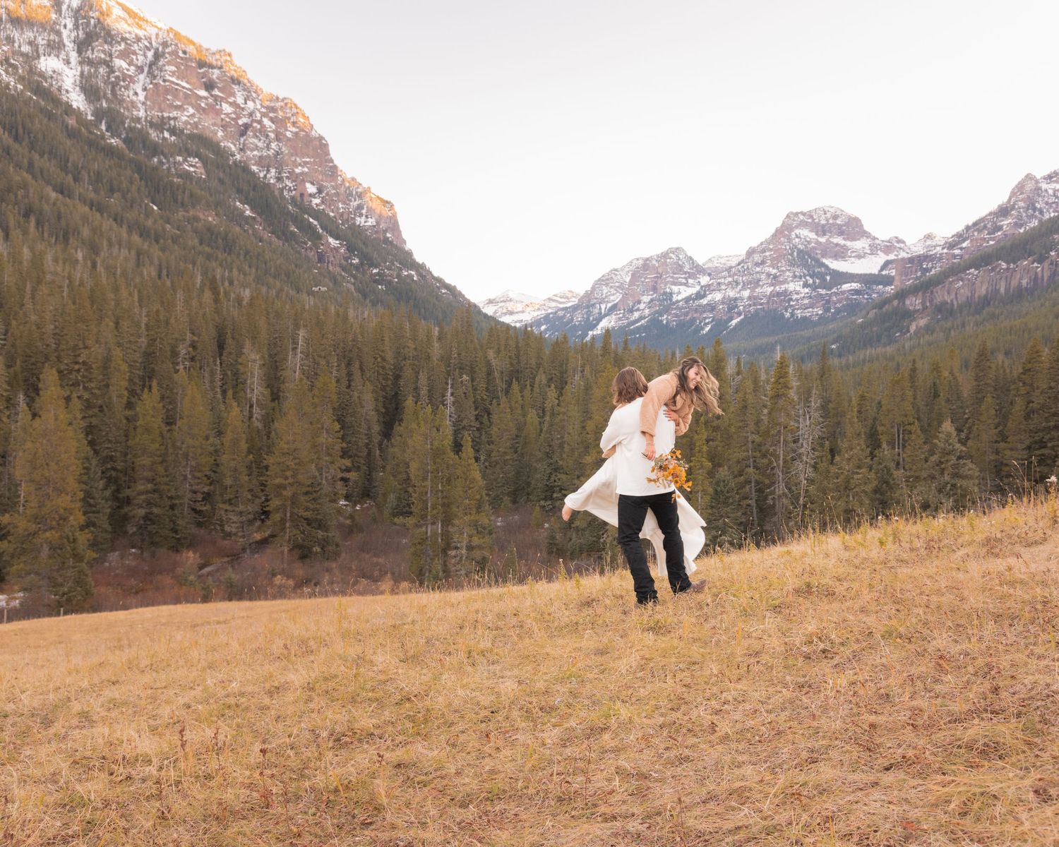 Dancing couple in a mountain valley surrounded by snow-capped peaks and evergreen forest.