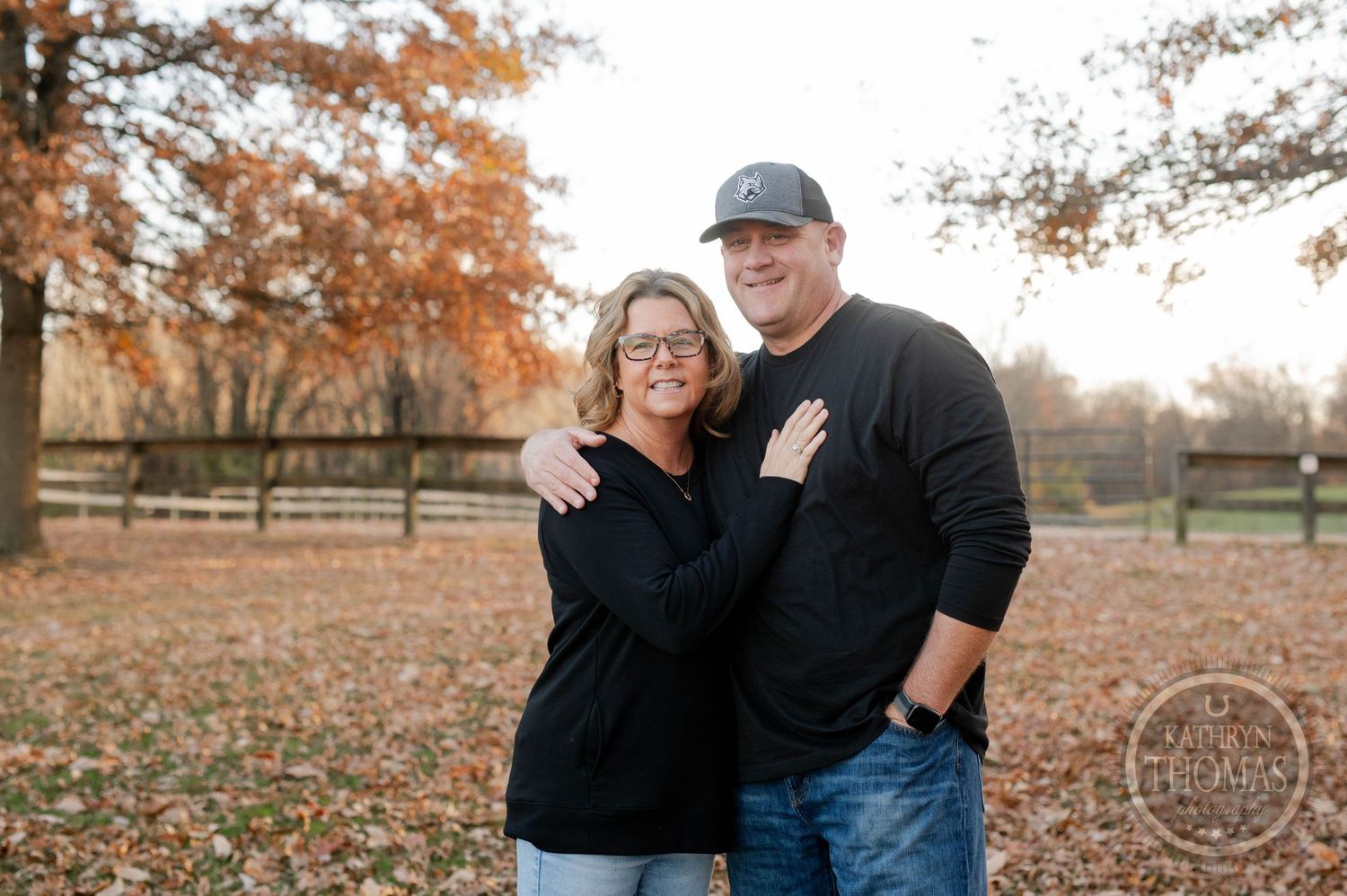 Couple shares a loving embrace while wearing matching black tops in an autumn setting.