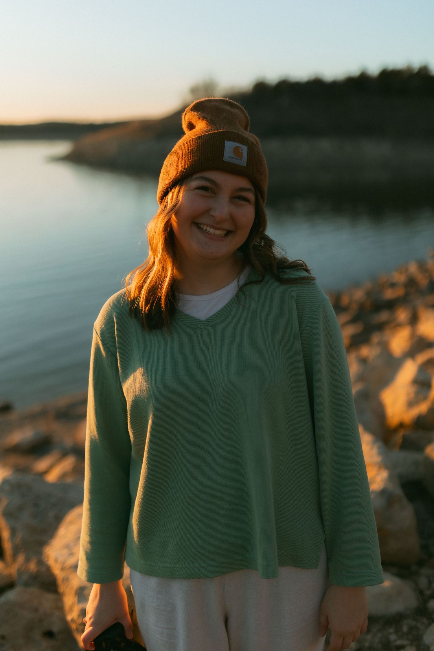 Emily Mae Photography looking off into the distance while holding a Canon R6 Mark ii camera. Smiling at golden hour