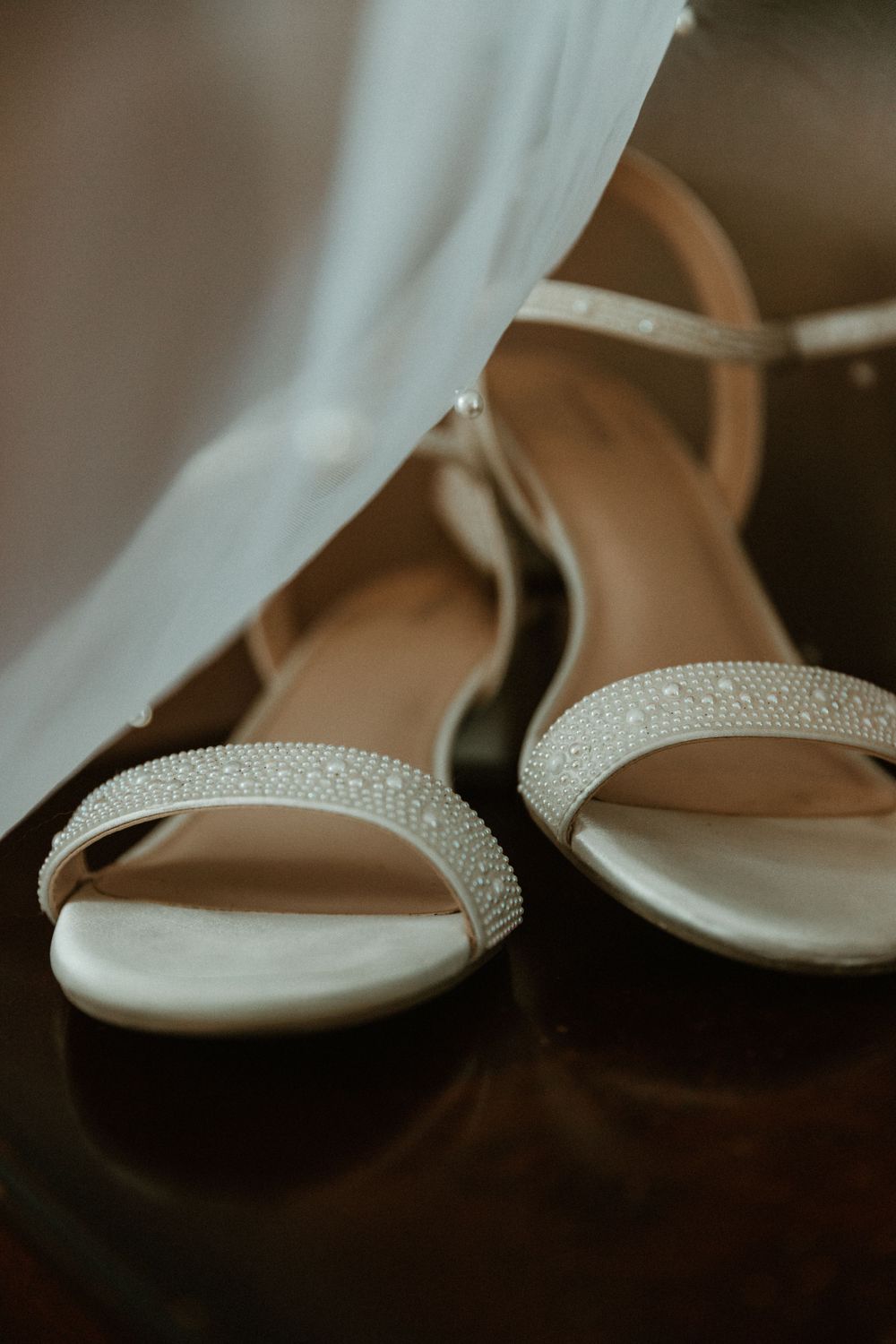 Close-up detail of elegant white bridal shoes with crystal embellishments on dark background.