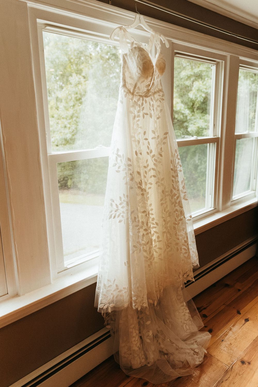 Wedding gown displayed by window with delicate lace details and flowing fabric.