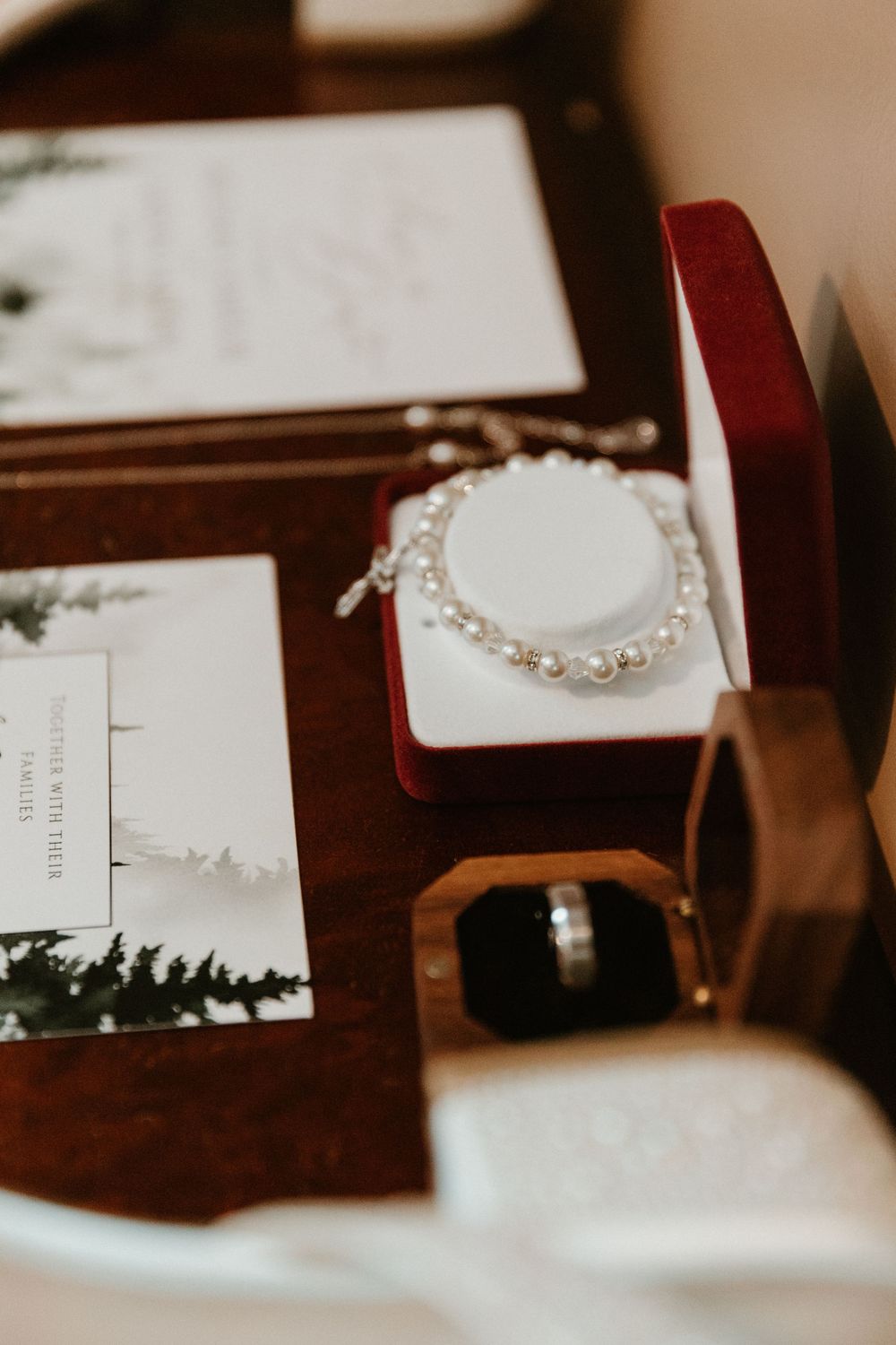 Pearl bracelet and wedding rings displayed with forest-themed wedding stationery.