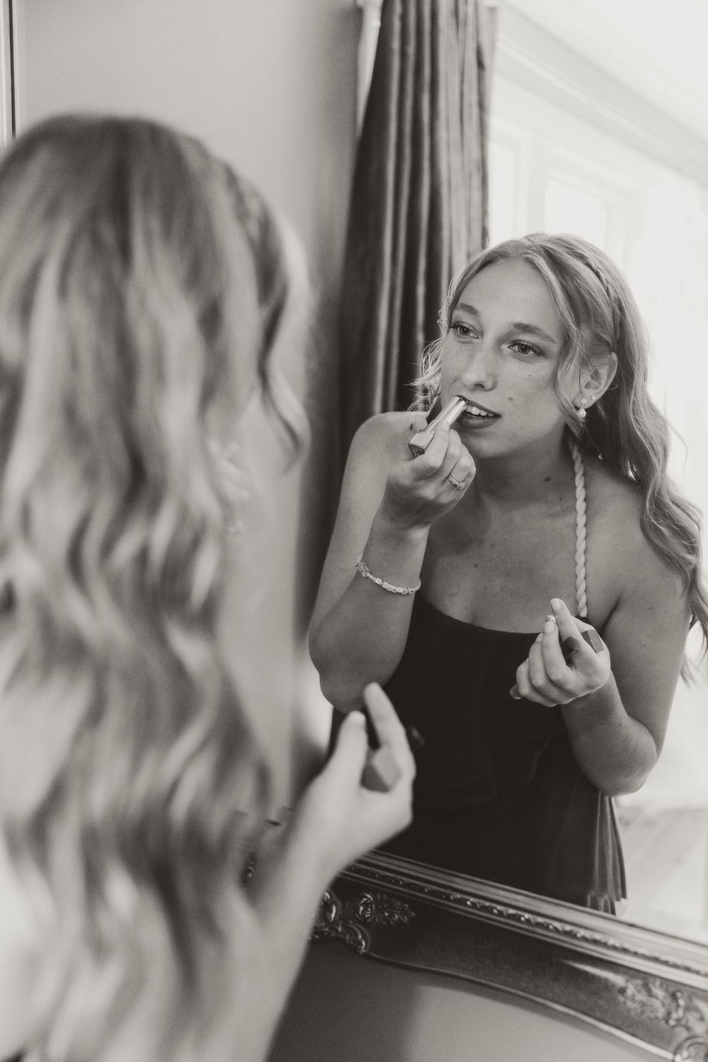 Person applying mascara in mirror during wedding day preparations.