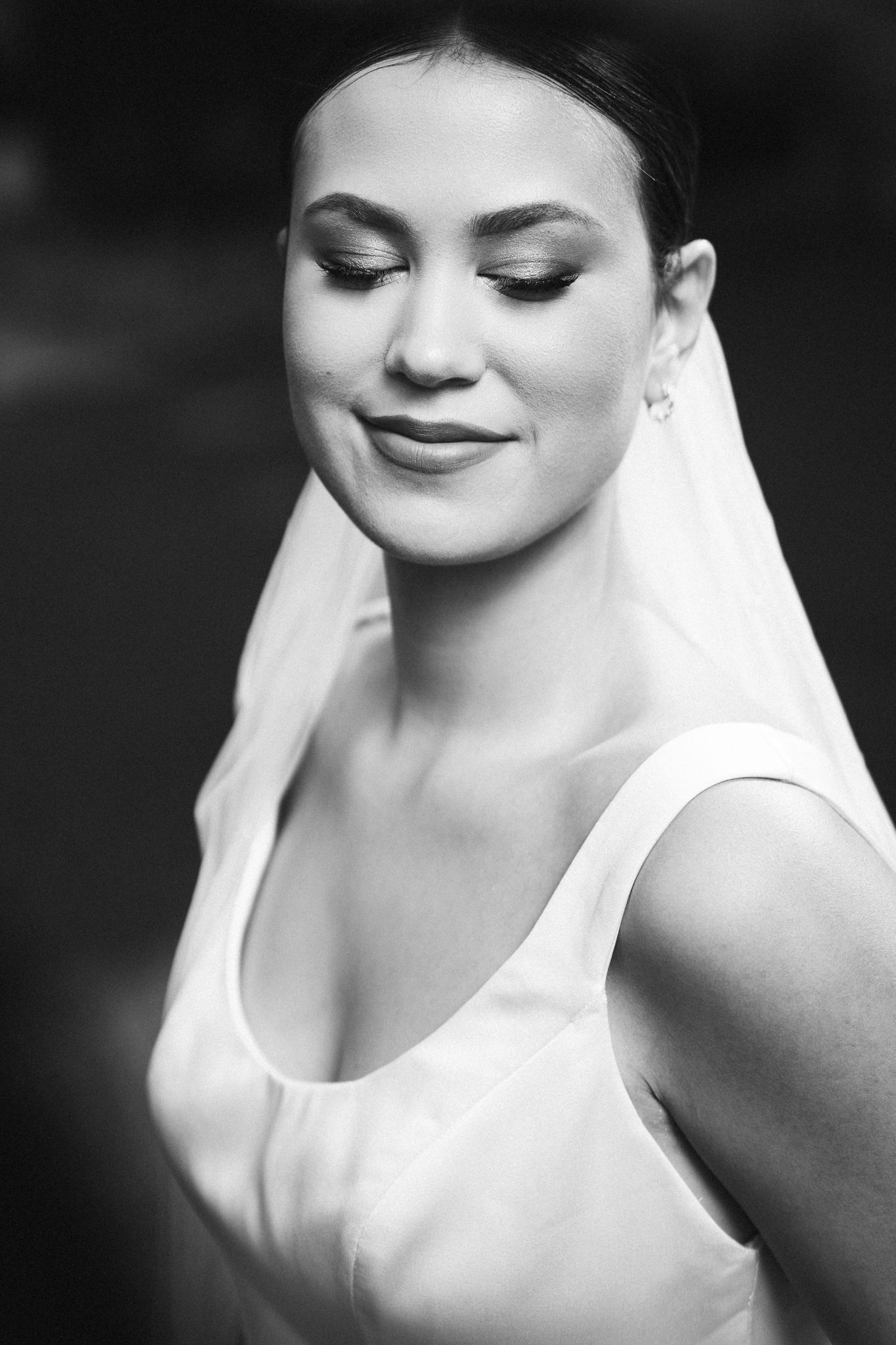 A black and white portrait of a bride in a minimalist dress with a flowing veil.