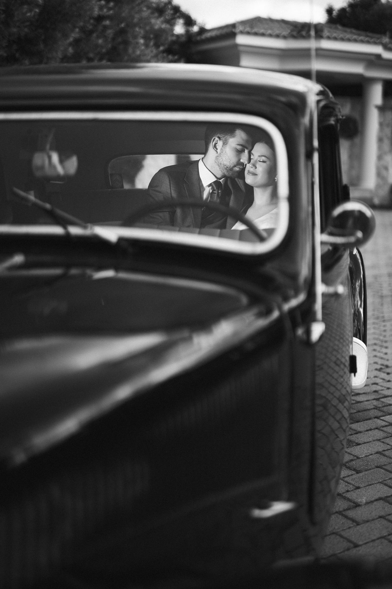 A romantic black and white photo of a couple sharing an intimate moment in a vintage car. naxt day wedding photoshoot.