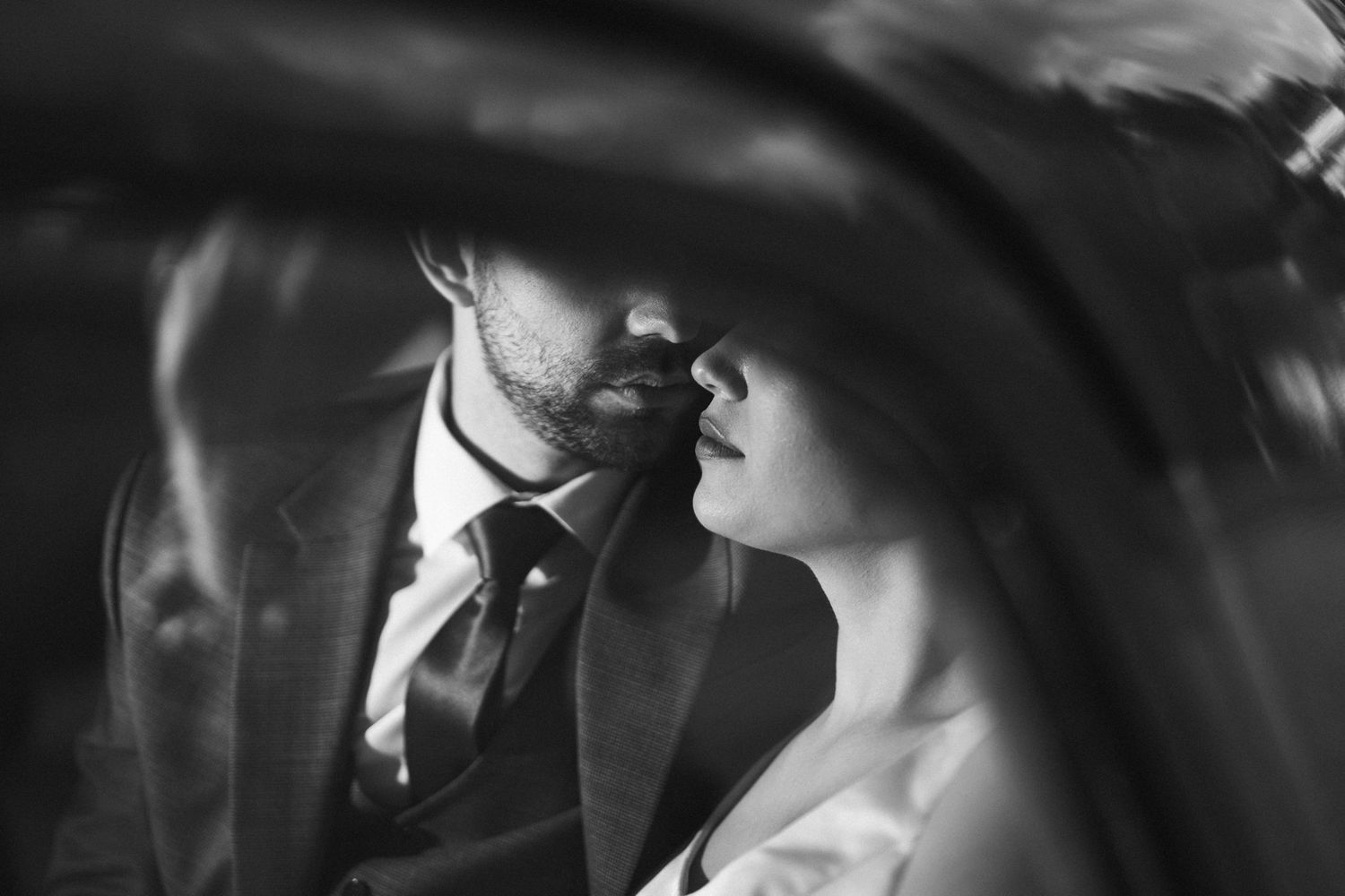 Intimate black and white moment captured through car window on wedding day.