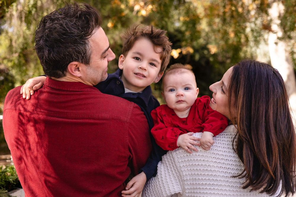 Close-up of mom, dad and two kids being held in between them as the parents look at each other warmly for holiday photos at Old Poway Park.