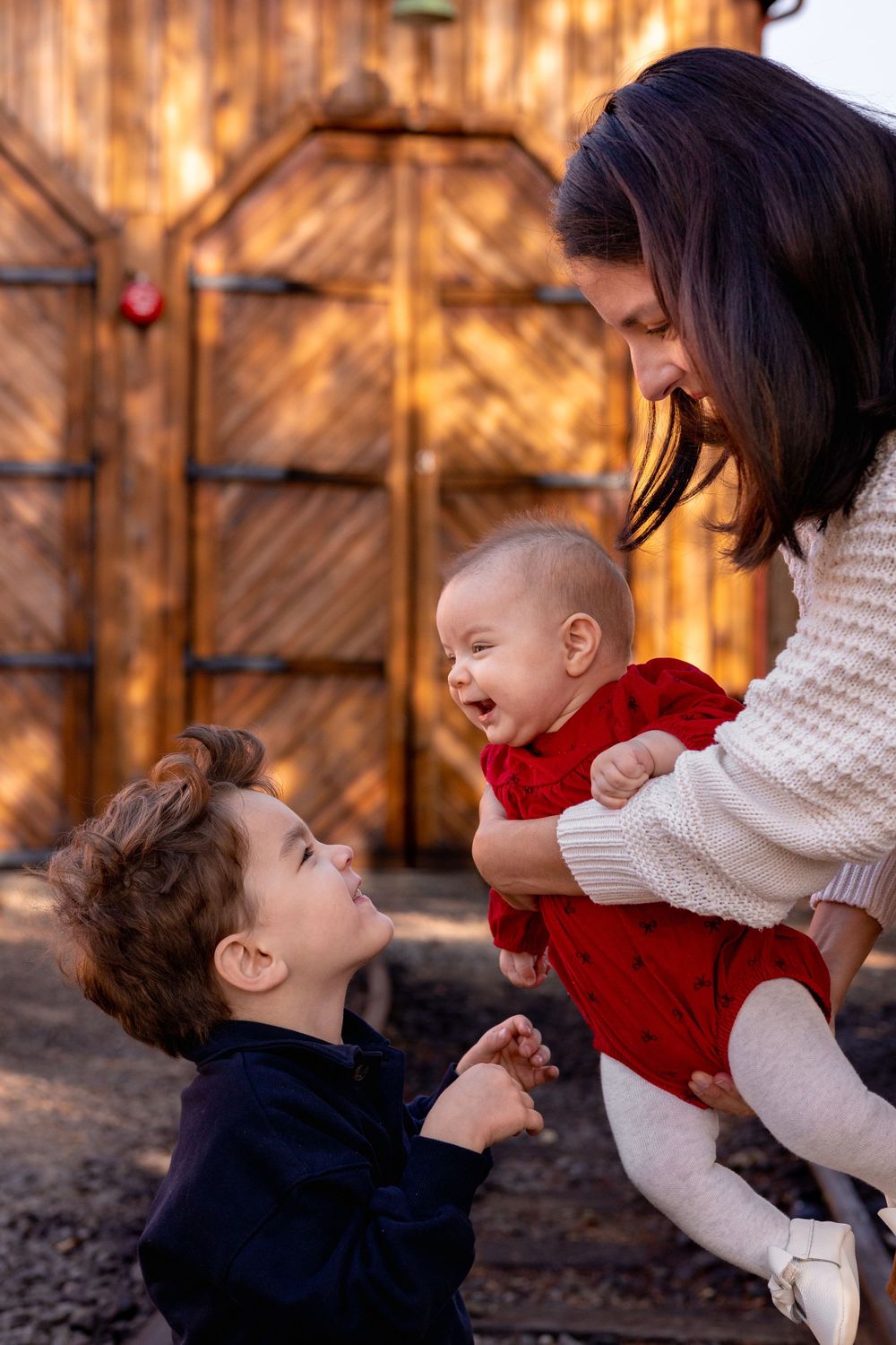Mom holds baby girl down towards big brother making a funny face at her to make her laugh. A special and intimate moment in motherhood.