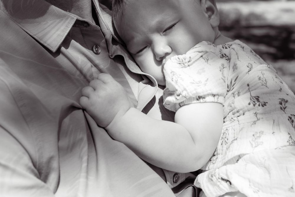 Black and white close-up of baby girl peacefully sleeping against dad’s chest in an intimate family moment in San Diego.