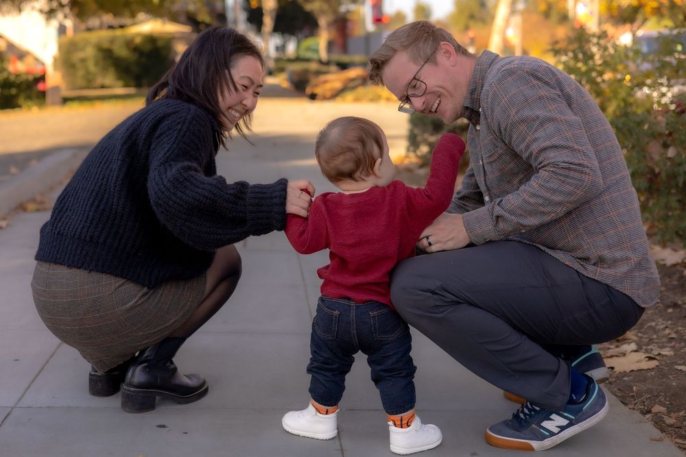 Parents crouched down laughing and looking at toddler boy with his back to camera during holiday session in Murrieta, CA.