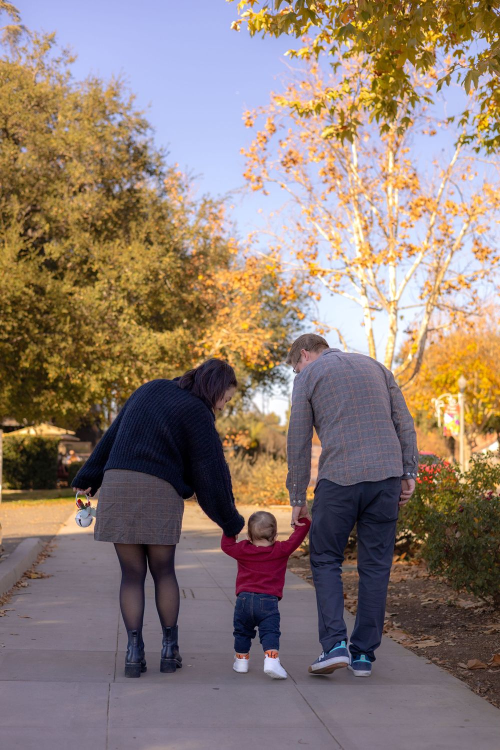Mom and dad holding toddler boy’s hands, backs to camera, walking away during holiday session in Murrieta, CA.
